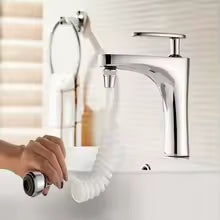 A modern chrome single-handle bathroom faucet with a flexible white hose attached, shown with a hand holding a small handheld device near the hose. The faucet is mounted on a white sink against a light beige tiled wall.